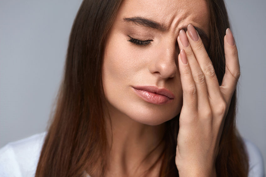 Frau mit Hand vor schmerzendem Auge